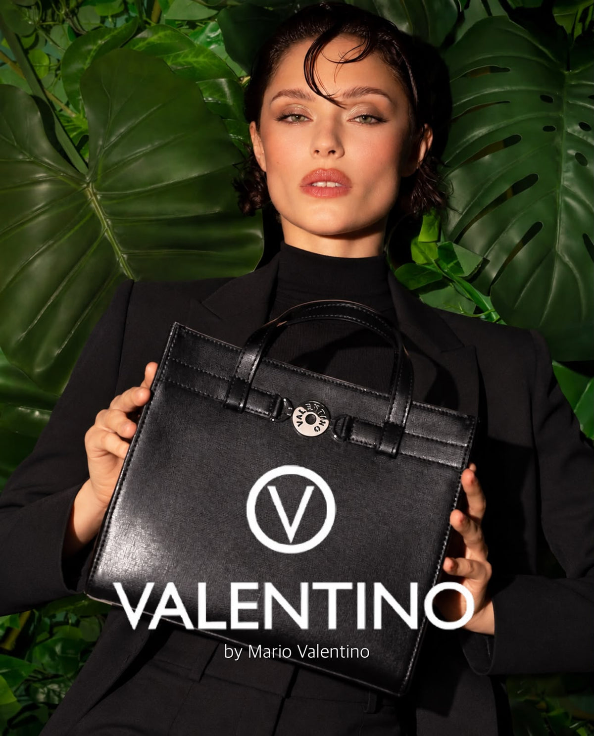 Model holding a black Valentino handbag in front of green leaves